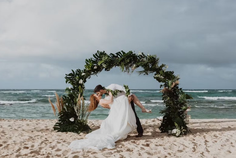 Married-couple-kissing-under-an-arbour-at-Hawaii-Polo-Club-beach-Wedding-Venue